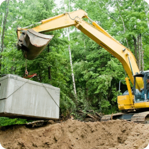 Excavator lowering a concrete septic tank into an excavated pit